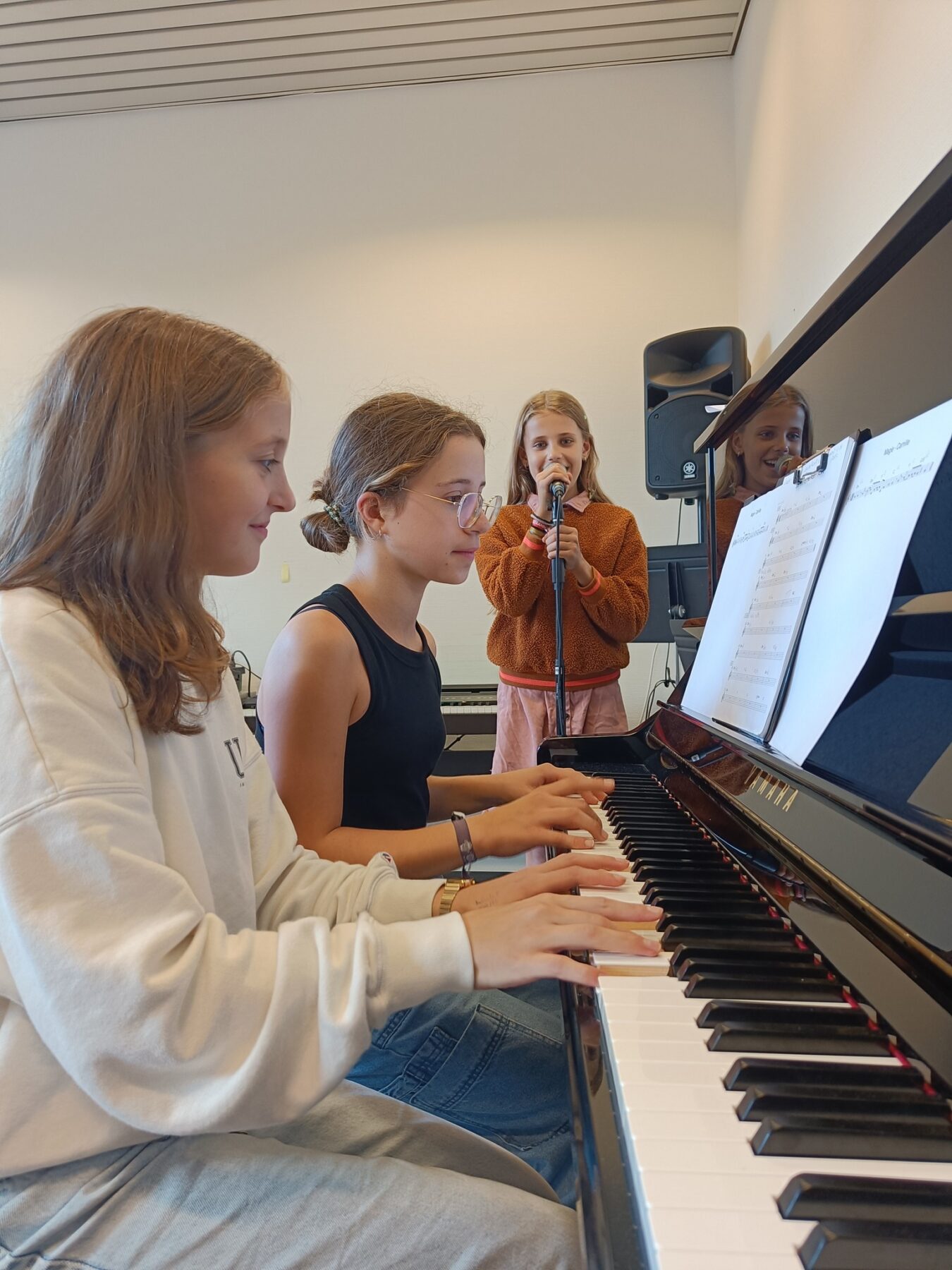 foto twee meisjes aan een piano een meisje met een microfoon
