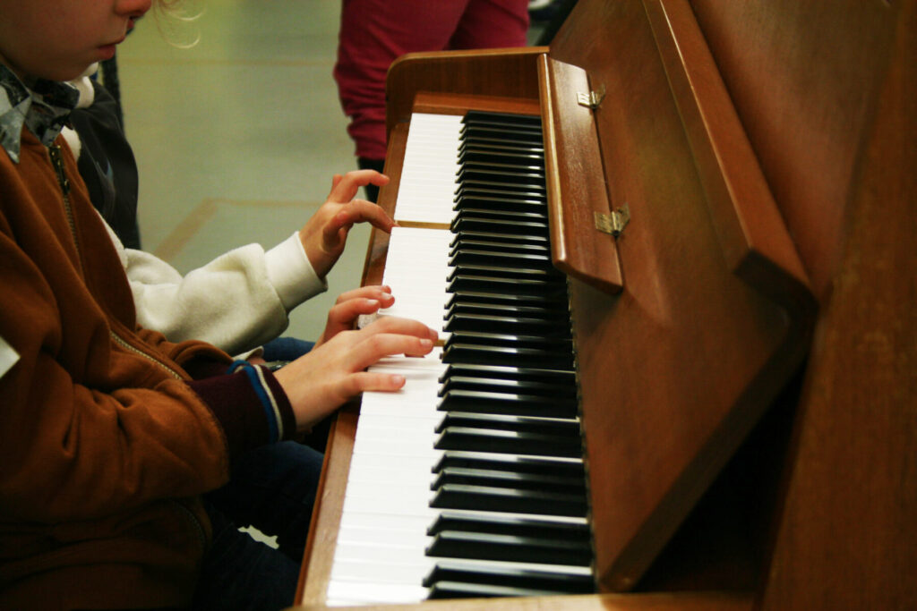 foto twee kinderen aan buffetpiano, je ziet enkel hun handen en armen